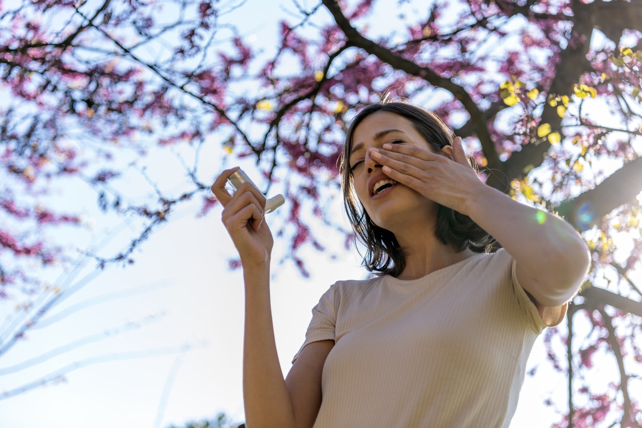 Woman with severe asthma holding an inhaler outside around trees