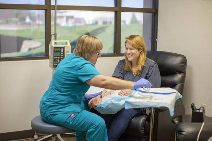 An IVX staff member setting a smiling woman up with her infusion